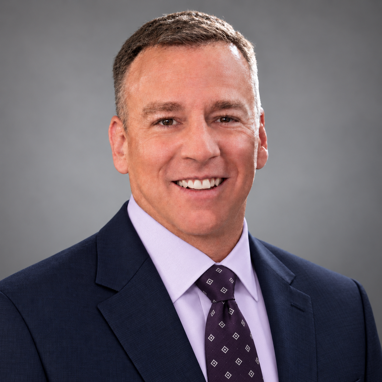 Greg Pliler — Website Headshot — Navy Suit, Lavender Shirt, Plum Tie Greg Pliler, Co-Founder and COO of GS Federal
